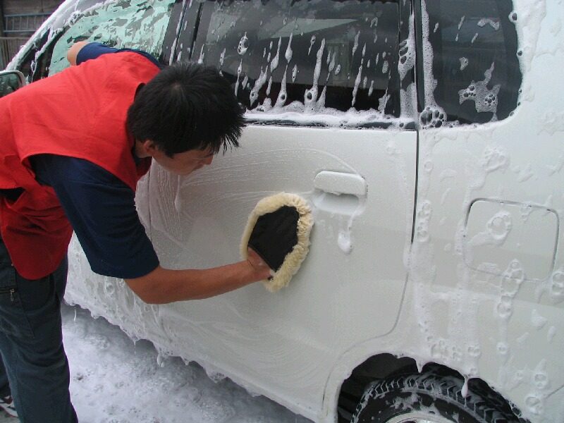 泡だらけの軽自動車を手洗いする